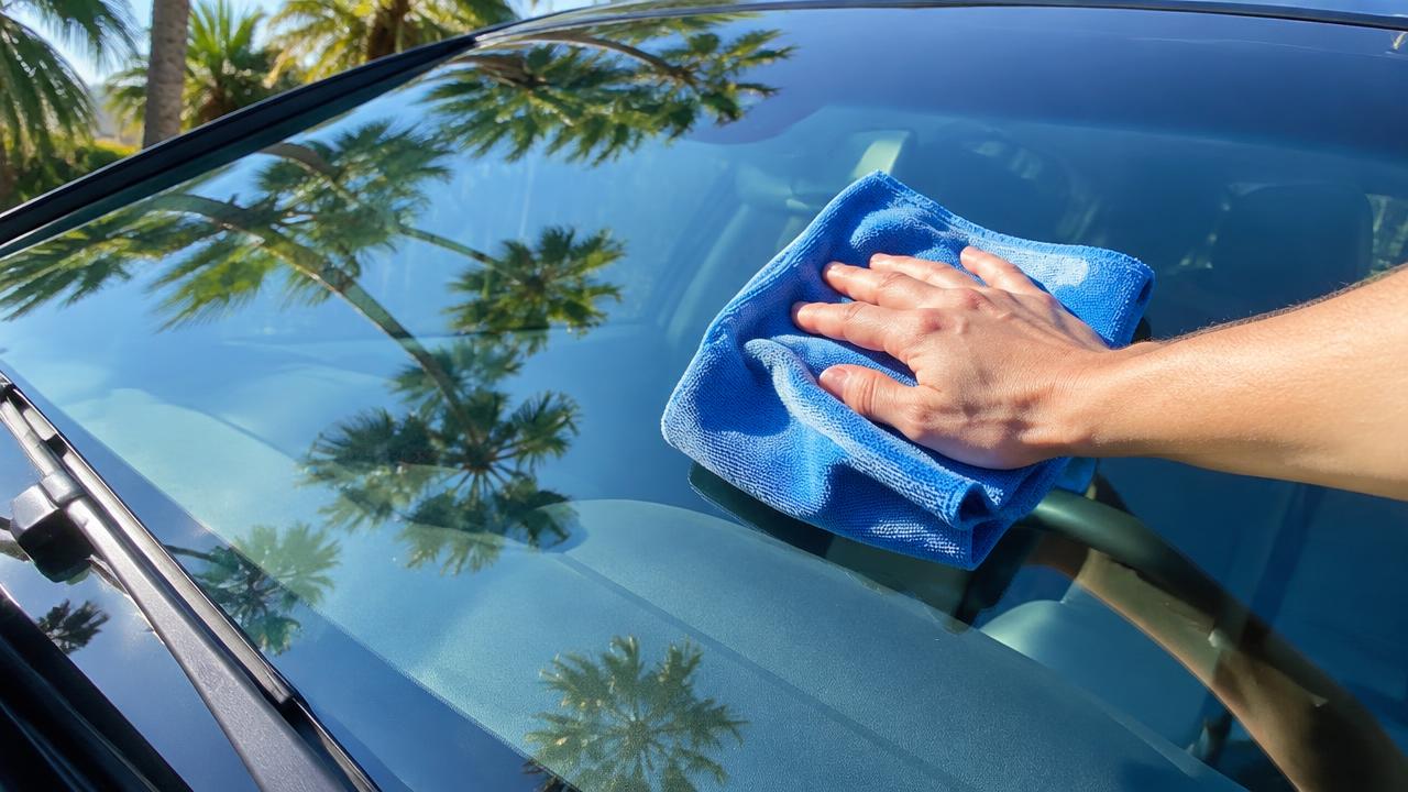 Microfiber towel cleaning a windshield with palm trees reflected in the glass